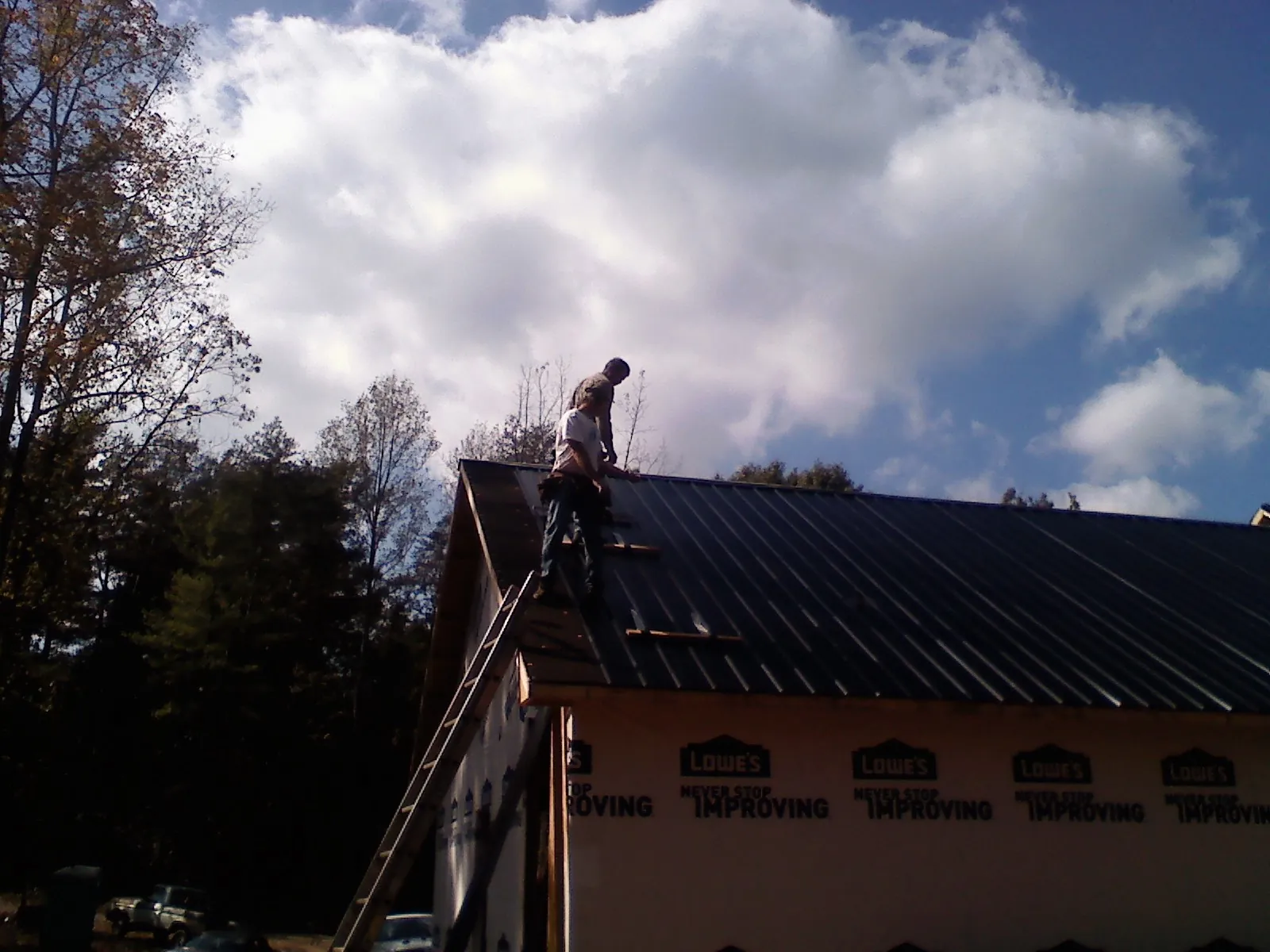 Roofer fastening dark metal panels high against a cloudy sky, from a Roof Inspection job in West Point